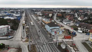 Luftaufnahme einer im Bau befindlichen Bahnstrecke. Die Gleise werden in einer Stadt mit vielen Gebäuden und Häusern verlegt. In der Nähe befinden sich Baufahrzeuge und ein blaues Gebäude.