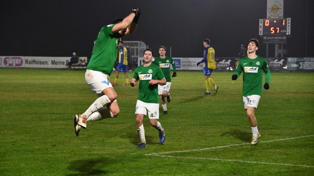Soccer players in green uniforms celebrate a goal on a field under night lights.