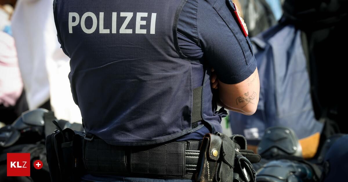 Ein Polizist steht mit dem Rücken zugewandt und zeigt das Wort 'POLIZEI' auf seiner Uniform. Er hat ein Tattoo auf seinem rechten Arm.