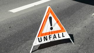 Ein orangefarbenes und weißes dreieckiges Warnzeichen mit dem Wort 'UNFALL' und einem Ausrufezeichen auf der Straße.