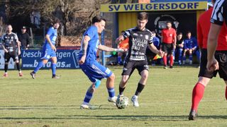 Zwei Fußballspieler, einer in Blau und der andere in Schwarz, sind in einem Fußballspiel auf einem Feld. Der Spieler in Blau versucht, den Ball zu kontrollieren, während der andere Spieler in Schwarz versucht, ihn zu stehlen.