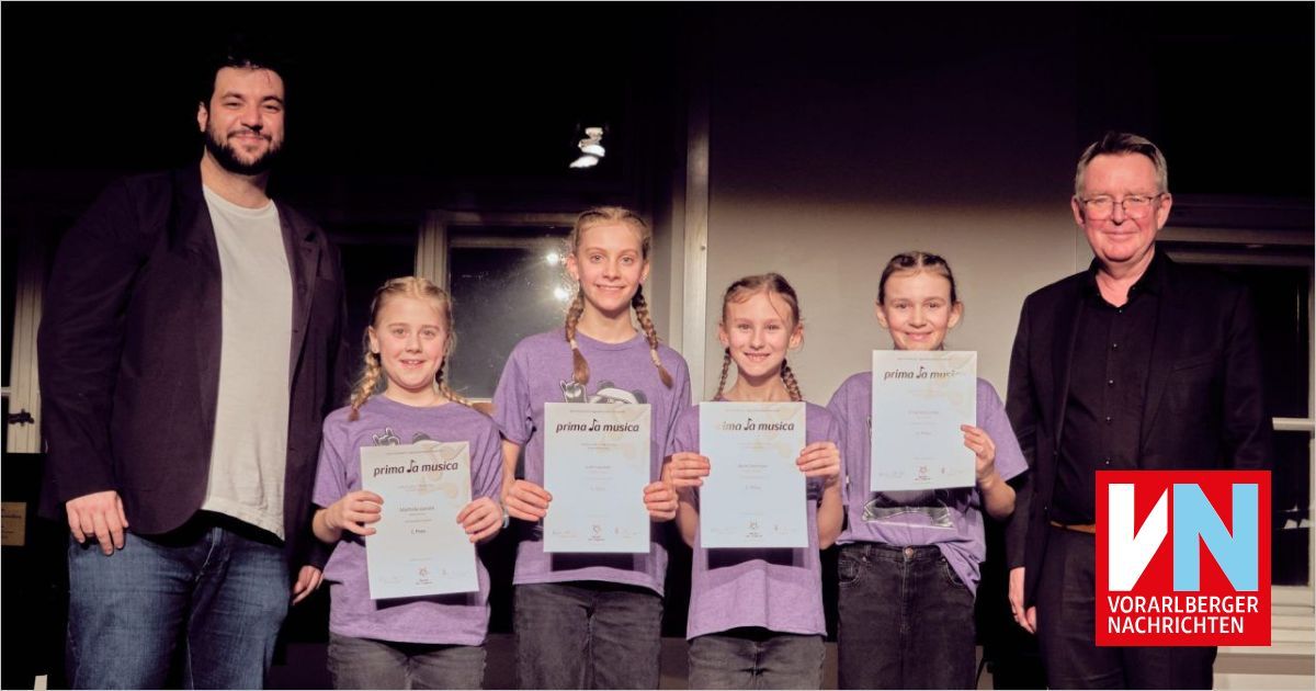 Fünf junge Mädchen, die Urkunden halten, posieren mit einem Mann für ein Foto, alle in lila Hemden gekleidet. Die Urkunden tragen die Worte 'prima la musica'. Dahinter befindet sich eine Wand mit einem Fenster.