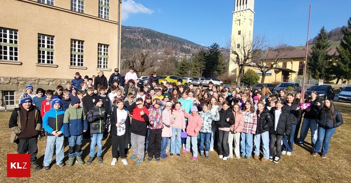 Eine große Gruppe von Kindern und Erwachsenen posiert für ein Foto vor einem Gebäude mit einem Uhrenturm und einem Berg im Hintergrund.
