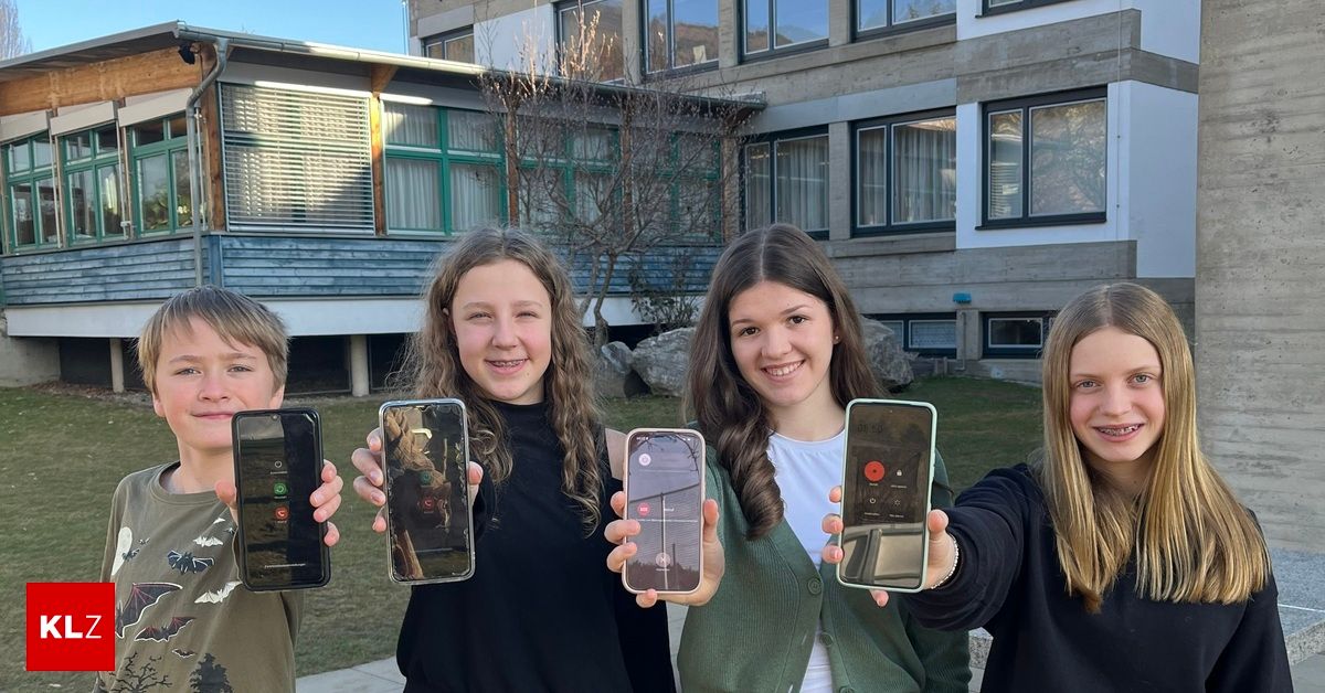 Vier Personen stehen vor einem Gebäude und halten Telefone hoch. Die beiden außen halten sie vertikal, während die beiden in der Mitte sie horizontal halten.