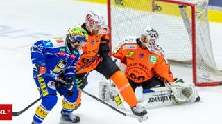 Drei Eishockeyspieler spielen auf einer Eisbahn. Zwei tragen orangefarbene Trikots, einer ist in Blau. Ein Spieler hält einen Hockeyschläger, während ein anderer vor dem Tor gekauert ist.