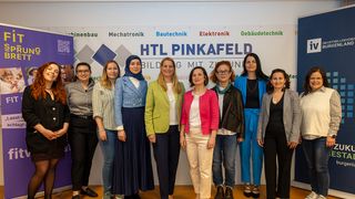 Eine Gruppe von Frauen steht vor einem Banner mit verschiedenen Ingenieursdisziplinen, darunter Mechatronik, Bauen mit Zukunft und Gebäudetechnik.