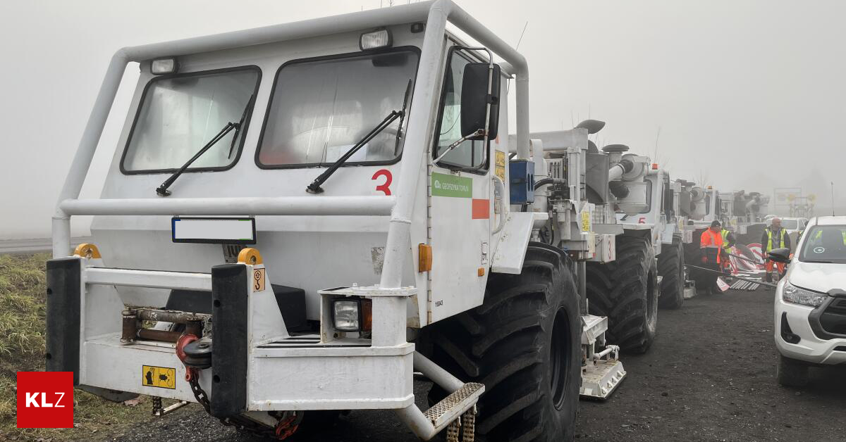 Eine Reihe großer weißer Fahrzeuge mit '3' auf der Vorderseite, auf einem staubigen Untergrund geparkt. Die Fahrzeuge haben große Reifen, einen grünen Aufkleber und ein Nummernschild.
