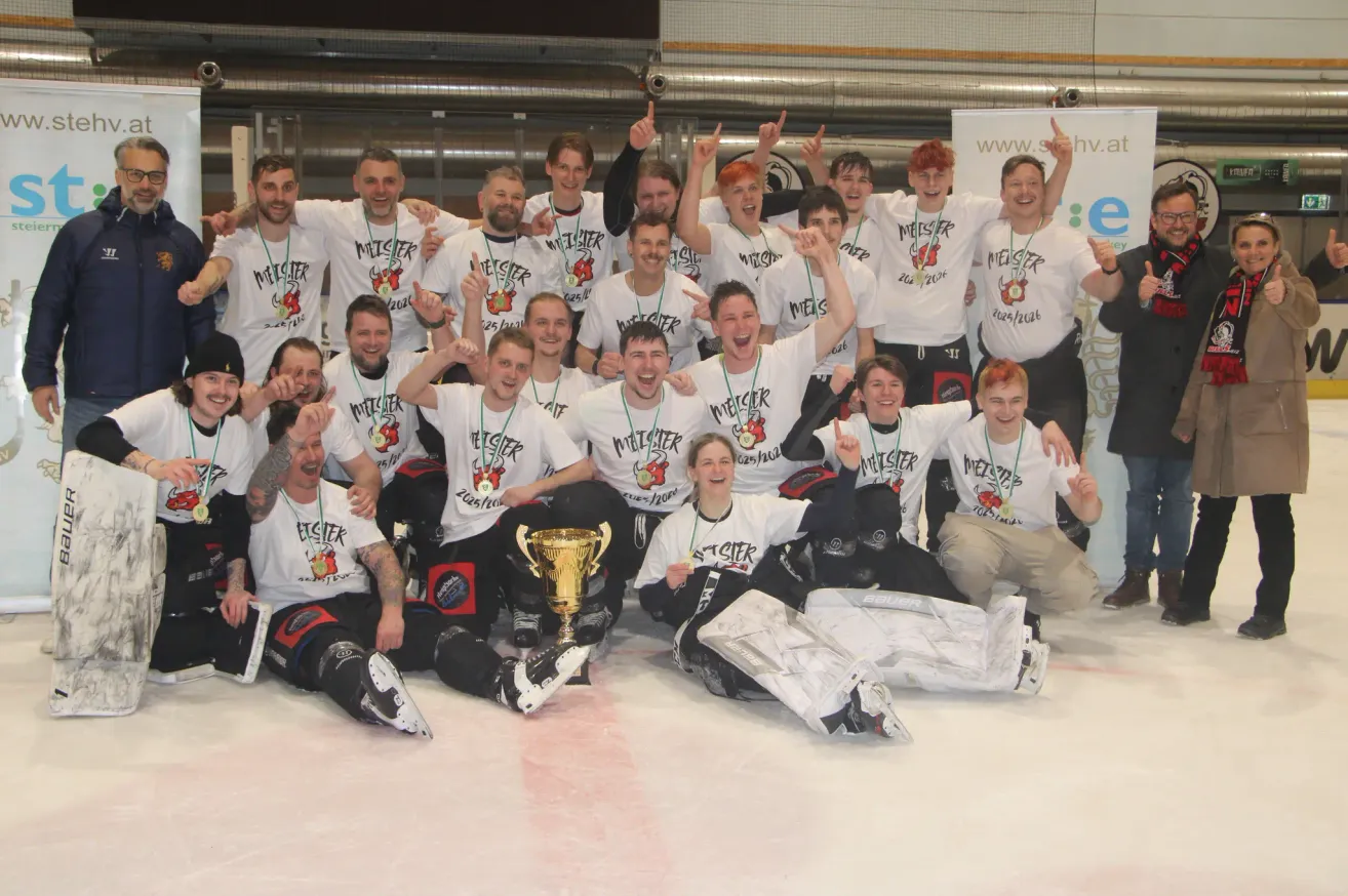 A group of men in white shirts and medals are posing for a photo on an ice rink. They are holding a trophy.