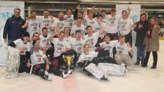 Eine Gruppe von Männern in weißen Hemden und Medaillen posiert für ein Foto auf einer Eisbahn. Sie halten einen Pokal.
