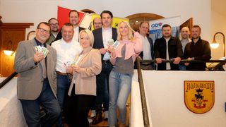 Eine Gruppe von Menschen, darunter Männer und Frauen, lächelt und posiert für ein Foto, während sie Karten in einem Raum halten.