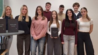 A group of young people standing in a line for a photograph, one holding a book titled 'Man of Values'.