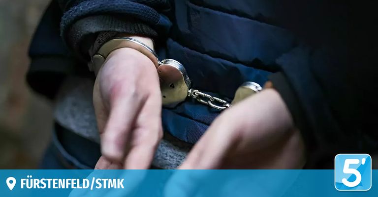 A person is handcuffed, wearing a blue jacket and a black shirt. The handcuffs are connected with a chain, and the person's hands are in front. The image has a watermark with the text 'ELD/STMK'.