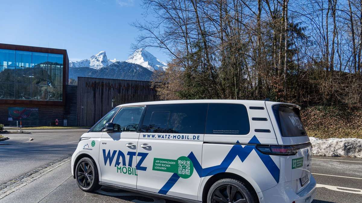 Ein weißer und blauer Watz Mobil Van geparkt vor verschneiten Bergen und Bäumen. An der Seite befinden sich 'WWW.WATZ-MOBIL.DE' und ein QR-Code.