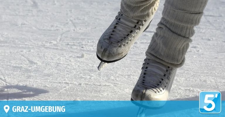 A person in ice skates is jumping on a snowy surface, wearing thick winter clothing.