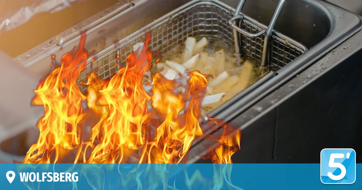 A fryer filled with oil is on fire, the flames engulfing the basket of fries. The oil is boiling and smoking.