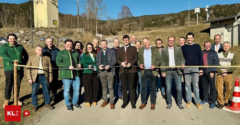 Eine Gruppe von Menschen in formeller Kleidung steht und hält eine gelbe Schleife für eine Schleifenschneidezeremonie auf einer Straße.