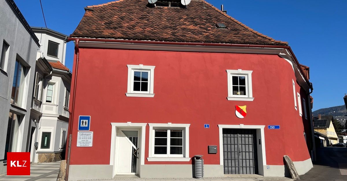 A red building with white windows and a coat of arms above the entrance. A trash bin is in front of the door.