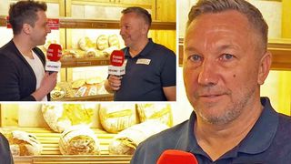 A man speaks into a microphone labeled Kronen Zeitung, with shelves of bread behind him. Another man is interviewed in front of a bread display.
