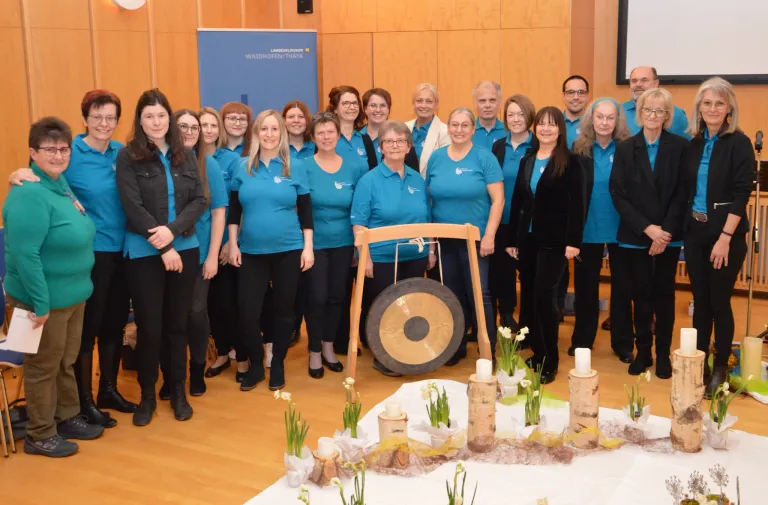 A group of people dressed in blue are posing for a photo with a gong and flowers on a table in front of them.