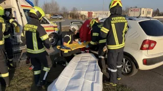 Firefighters in protective gear work on a stretcher, with one individual wearing gloves. A car is visible in the background.