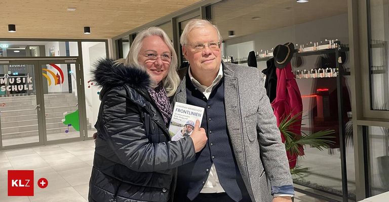 A man and a woman in winter clothes stand in a room holding a book titled Christian Front Lines.