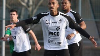 A soccer player wearing a white and black jersey with the word 'MCE' on the front, standing in a field.