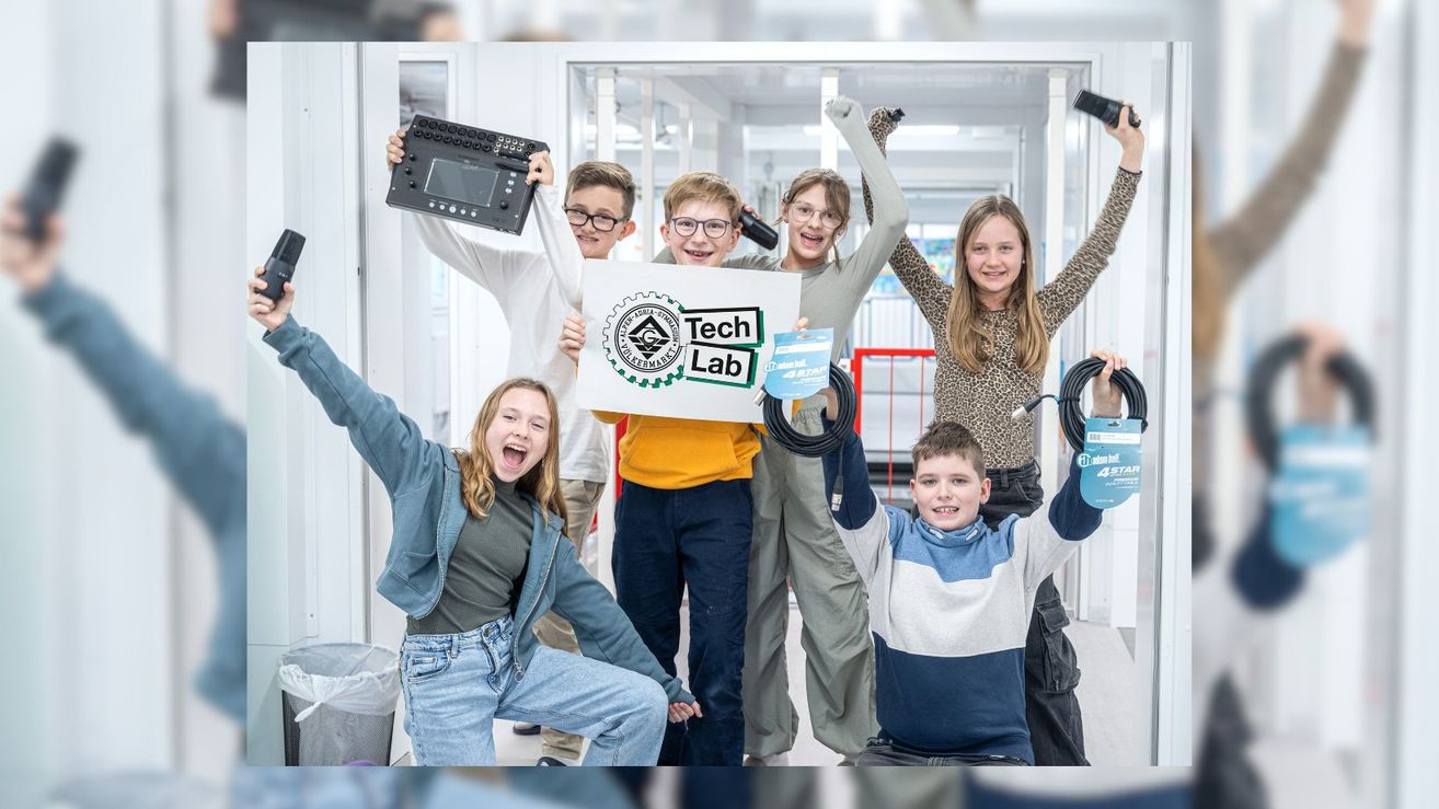 Group of children posing for a photo in a Tech Lab, holding a sign, electronic devices, and cables, with a cheerful and excited atmosphere.