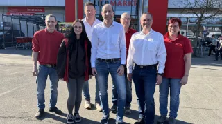 Eine Gruppe von sechs Personen steht vor einem Liebmarkt-Laden, alle tragen rote Hemden und lächeln für ein Foto.