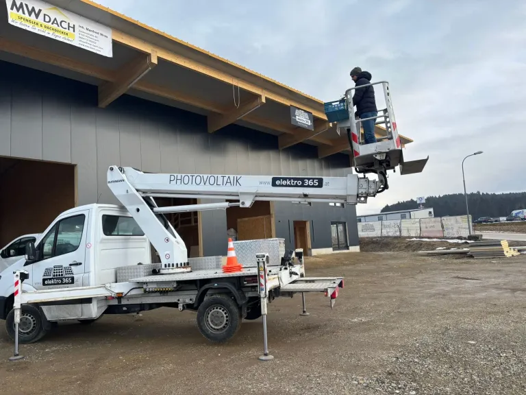 A person is using a white elektro 365 crane on a truck to work on a building under construction.