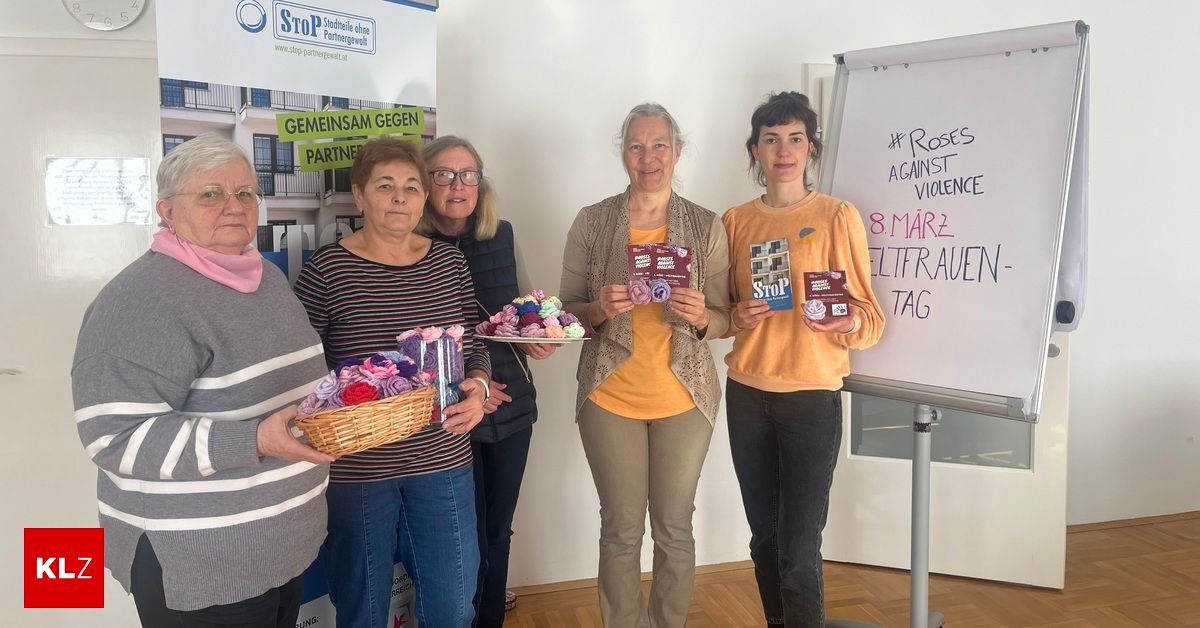 Five women hold baskets and pamphlets, standing before a whiteboard with '#Roses Against Violence 8 March Weltfrauen Tag' written on it. They are likely attending an event for International Women's Day.