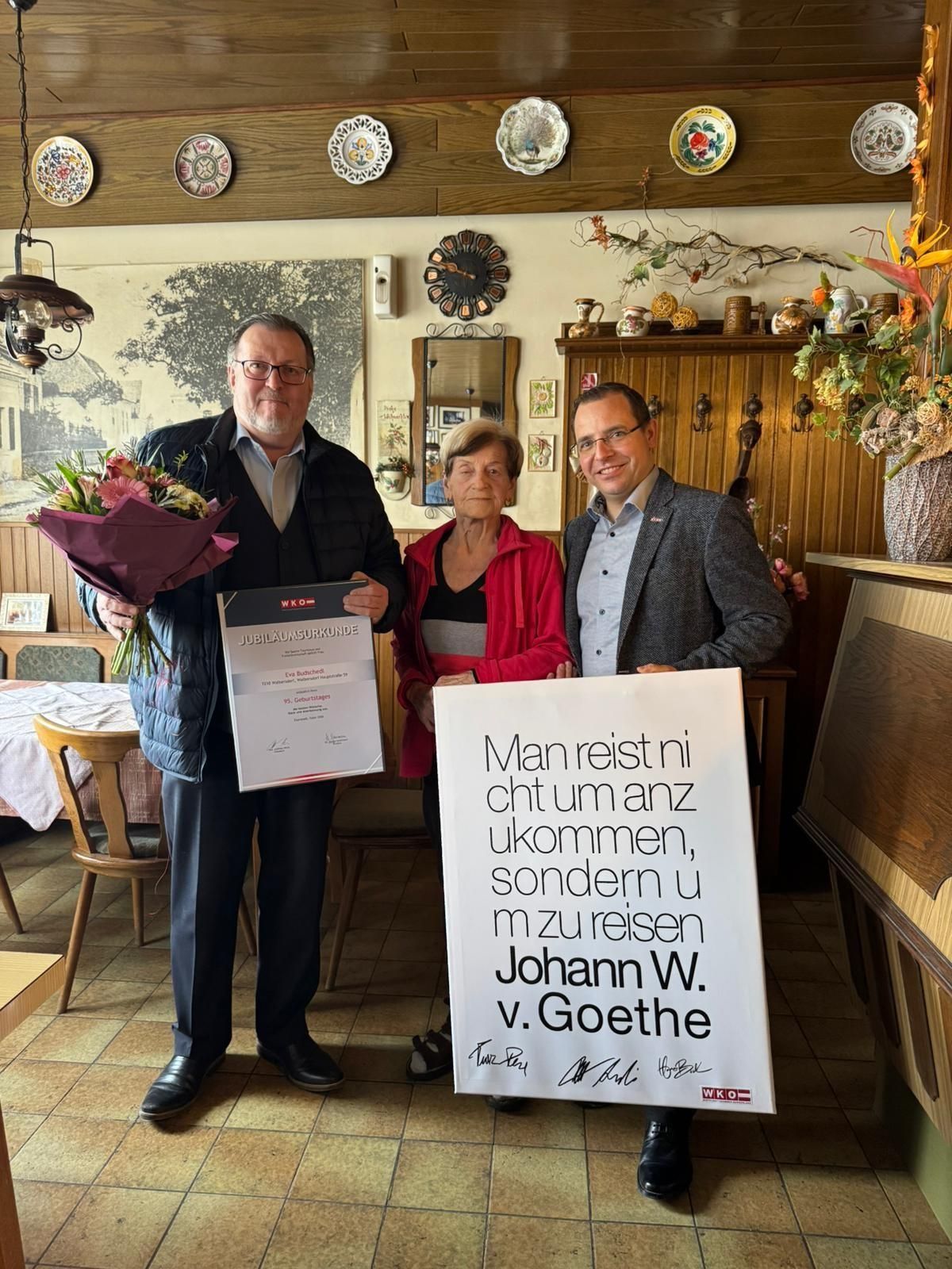 Three people are standing in a room. A man on the left is holding a bouquet of flowers. A woman and a man are standing beside him. They are all smiling.