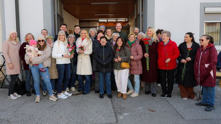 A group of people are posing for a photo while holding red roses in front of a building.