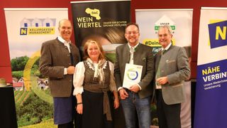 Four people are standing next to each other and smiling. They are holding a certificate with the name Thomas Weiderth. They are in front of a banner with the text Wein Viertel and DAC.