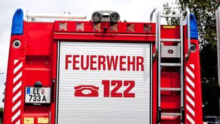A close-up of a red fire truck with the word 'FEUERWEHR' and the number '122' on its door. Above the door, there are several lights.