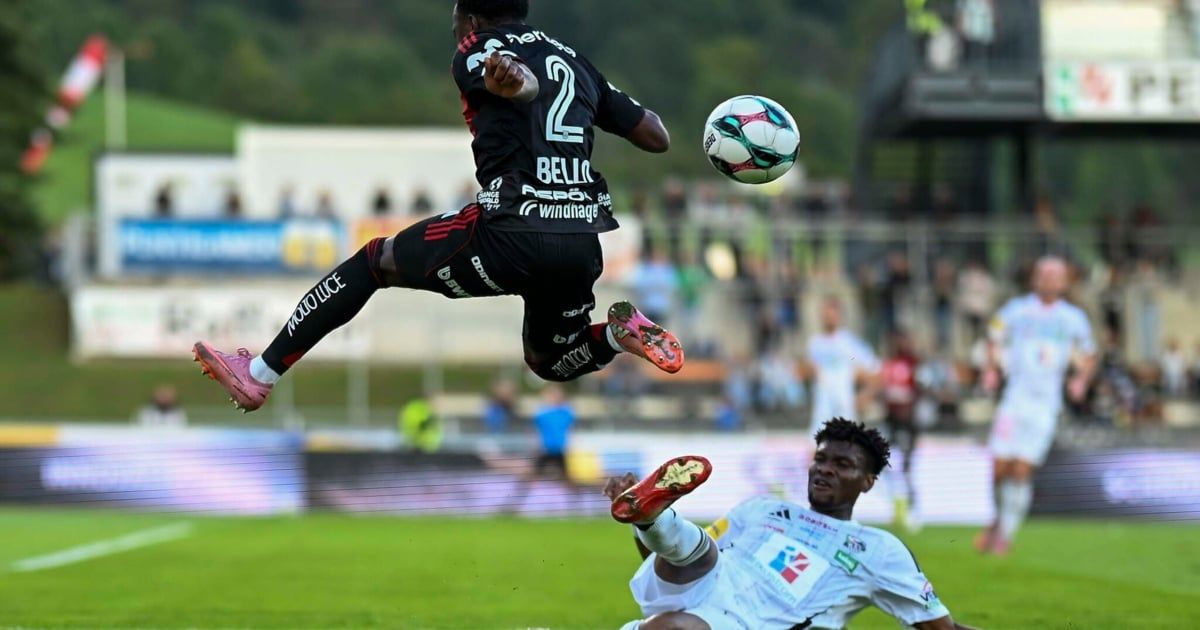 A soccer player in black jersey number 2 jumps to head the ball, while another player in white jersey looks on.