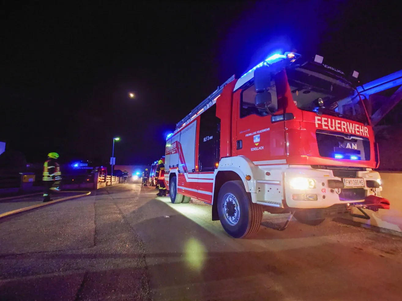 A red fire truck with its lights on is parked on the side of the road at night.