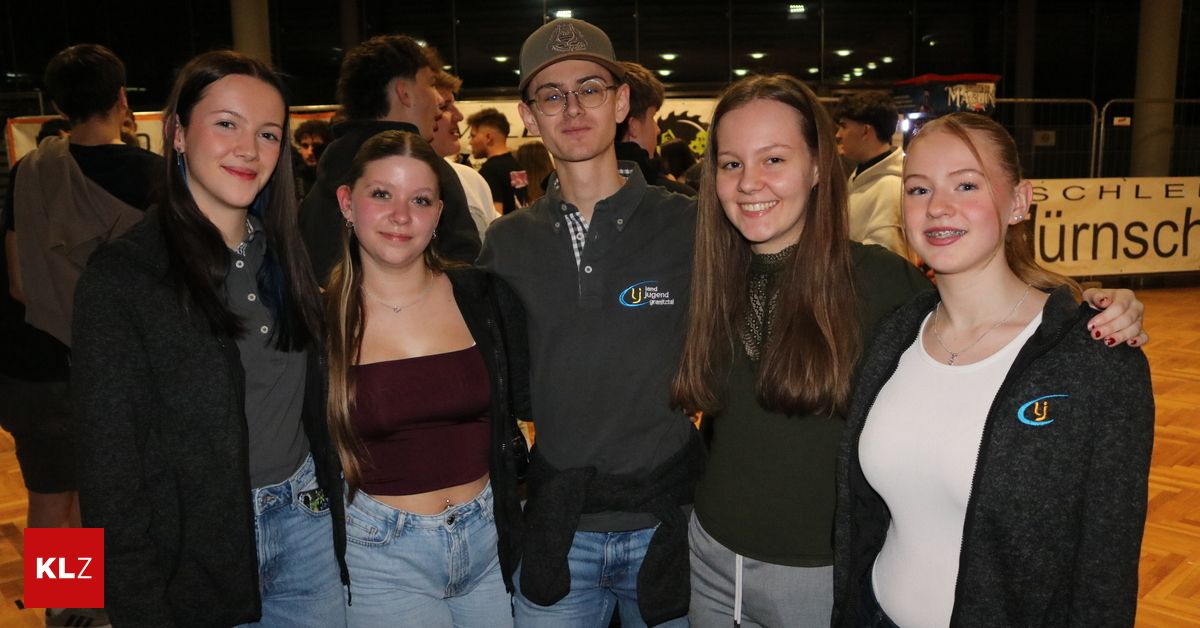A group of young people are posing for a picture, with one wearing a cap and glasses, another in a maroon crop top, and others in various colored tops.
