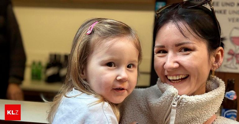 Eine Frau und ein junges Mädchen lächeln und schauen in die Kamera. Das Mädchen hat Zöpfe. Sie stehen eng beieinander.