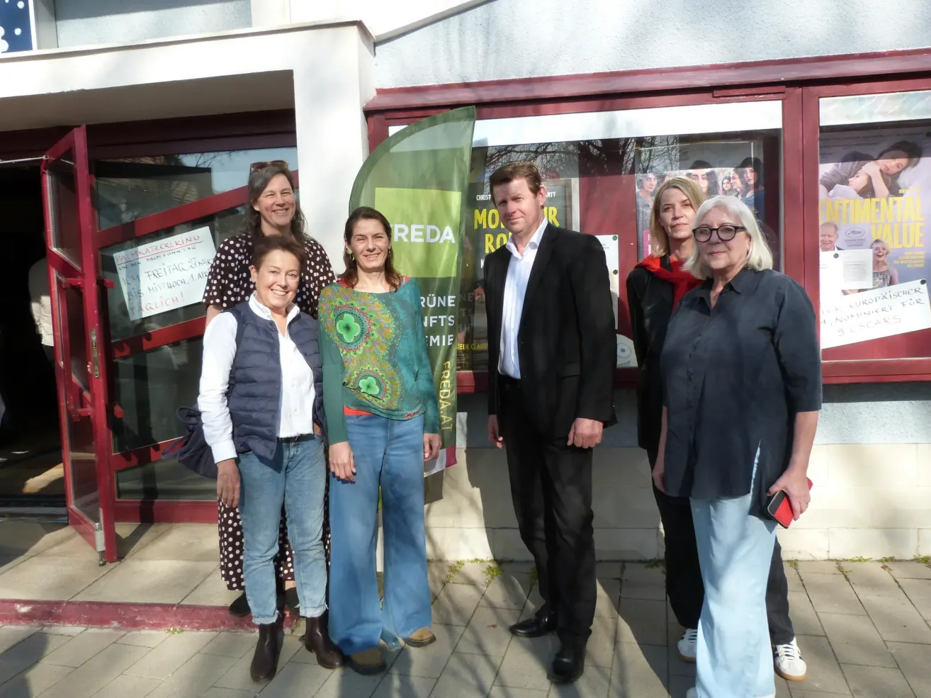 A group of six people pose for a photo outside a building. A banner with the word 'REDA' is held by one of them.