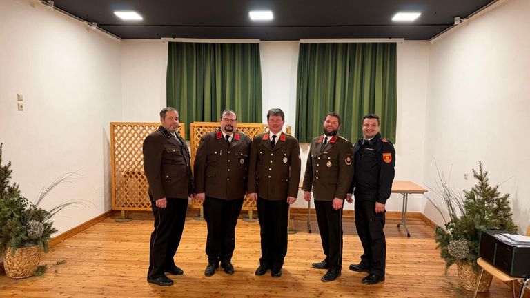 Fünf Männer in Uniformen stehen in einem Raum mit Holzboden. Grüne Vorhänge sind hinter ihnen.