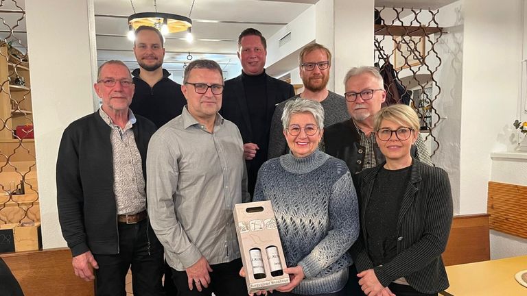 A group of people, including a woman holding a box of wine, are posing for a photo in a room.