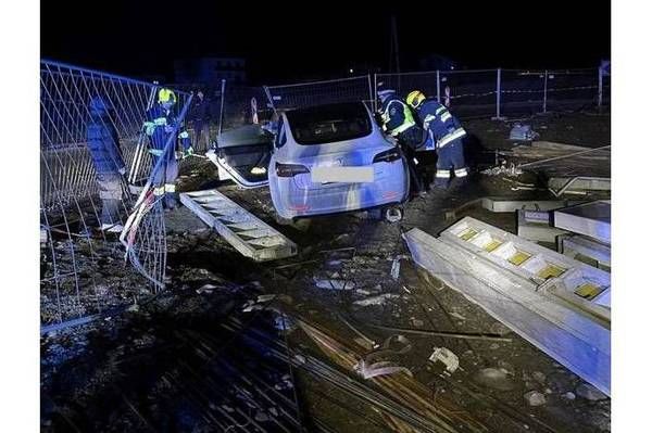 Notfallhelfer bei Nacht unterstützen ein beschädigtes Auto. Das Fahrzeug steht seitlich gegen einen Zaun, mit offener Tür.