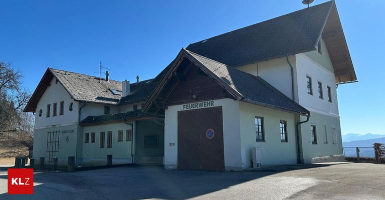 A fire station building with a brown door and a sign that reads Feuerwehr. The building has a chimney and several windows.