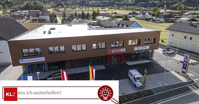 Ein Luftbild eines modernen Gebäudes mit Fahnen davor. Das Gebäude hat ein Schild mit den Aufschriften 'SPAR' und 'ZADUGA'. Vor dem Gebäude sind Autos geparkt. Ein weißer Lieferwagen ist auf der rechten Seite geparkt.