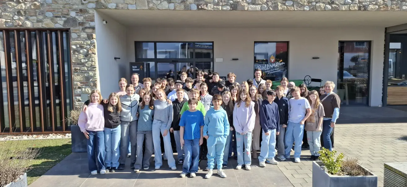 Eine Gruppe von Schülern und einigen Erwachsenen posiert für ein Foto vor einem Gebäude mit Glasfenstern.