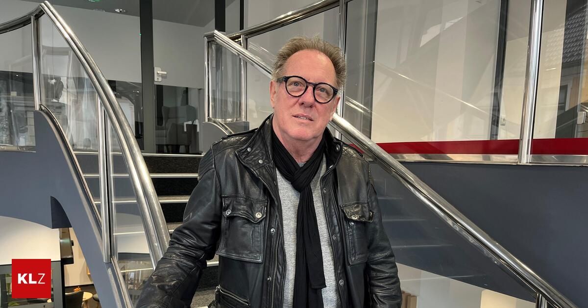 Ein Mann in einer schwarzen Lederjacke und einem Schal steht auf einer Treppe mit einem Metallgeländer.