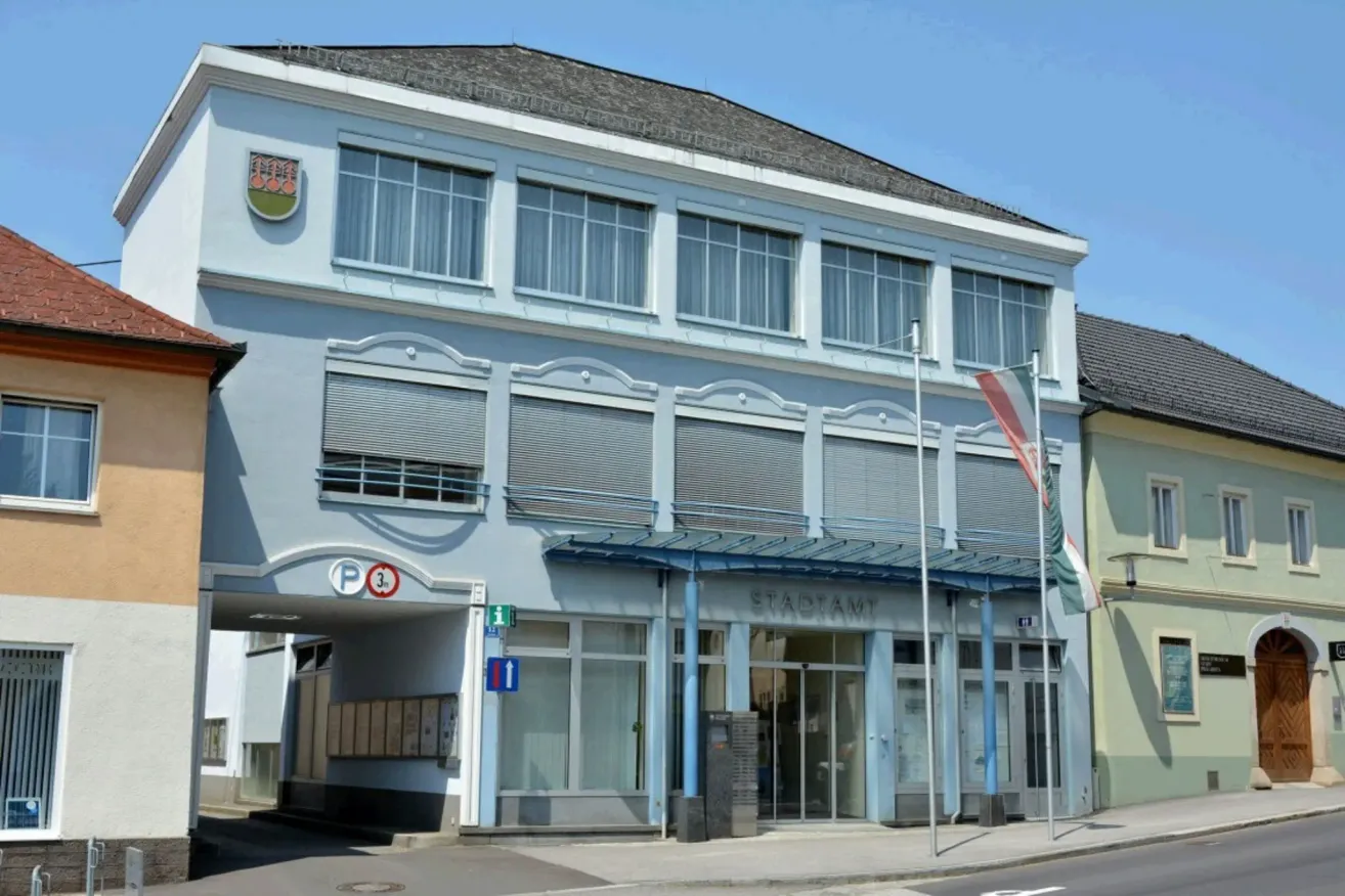 Die Vorderseite eines weißen Gebäudes mit einer Flagge auf einem Pfosten. Das Gebäude hat Glasfenster und Türen. Das Gebäude hat ein Schild, das 'STADIAM' besagt.