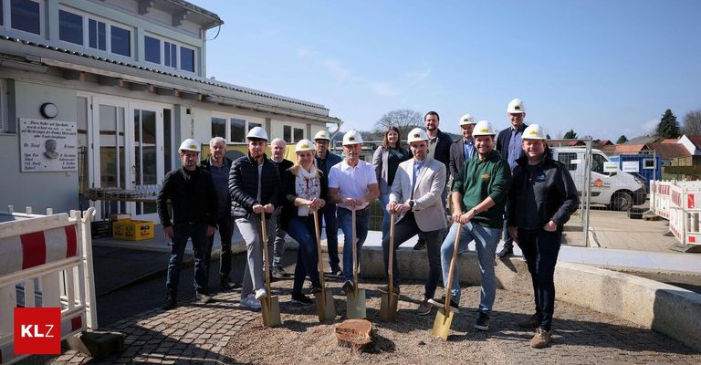 Eine Gruppe von Menschen, darunter Männer und Frauen, versammelt sich im Freien vor einem Gebäude. Sie tragen weiße Helme und halten Schaufeln in der Hand und posieren für ein Foto.