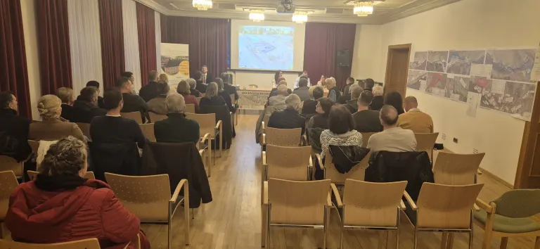 Eine laufende Konferenz mit einer Gruppe von Personen, die in Reihen sitzen und einer Präsentation auf einer Projektionsleinwand zuhören.