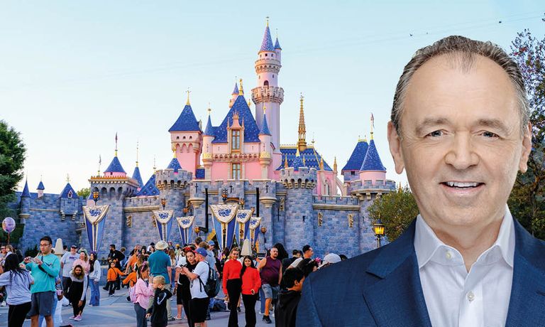 Ein lächelnder Mann steht vor dem Disneyland-Schloss, während viele Besucher in der Gegend herumlaufen.